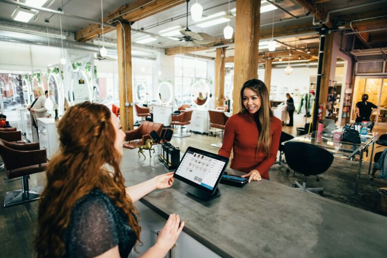 Two women sitting at a wooden counter in a cafe, looking at a tablet