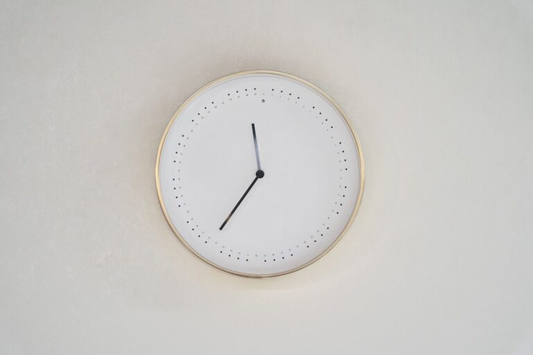 A plain wall clock with no numbers on a pale wall