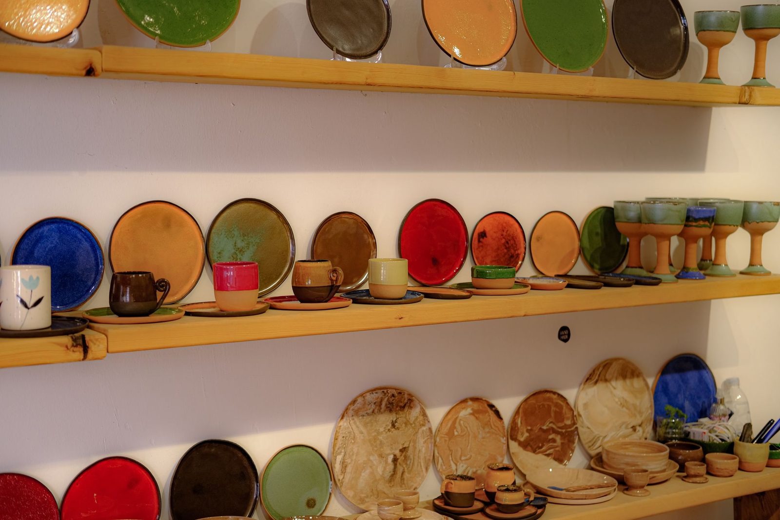 Handmade ceramic plates and cups on wooden shelves in a small shop