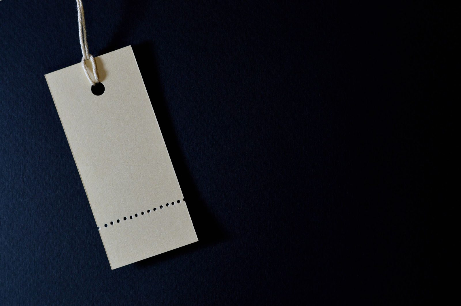 A blank paper price tag on a string against a dark background