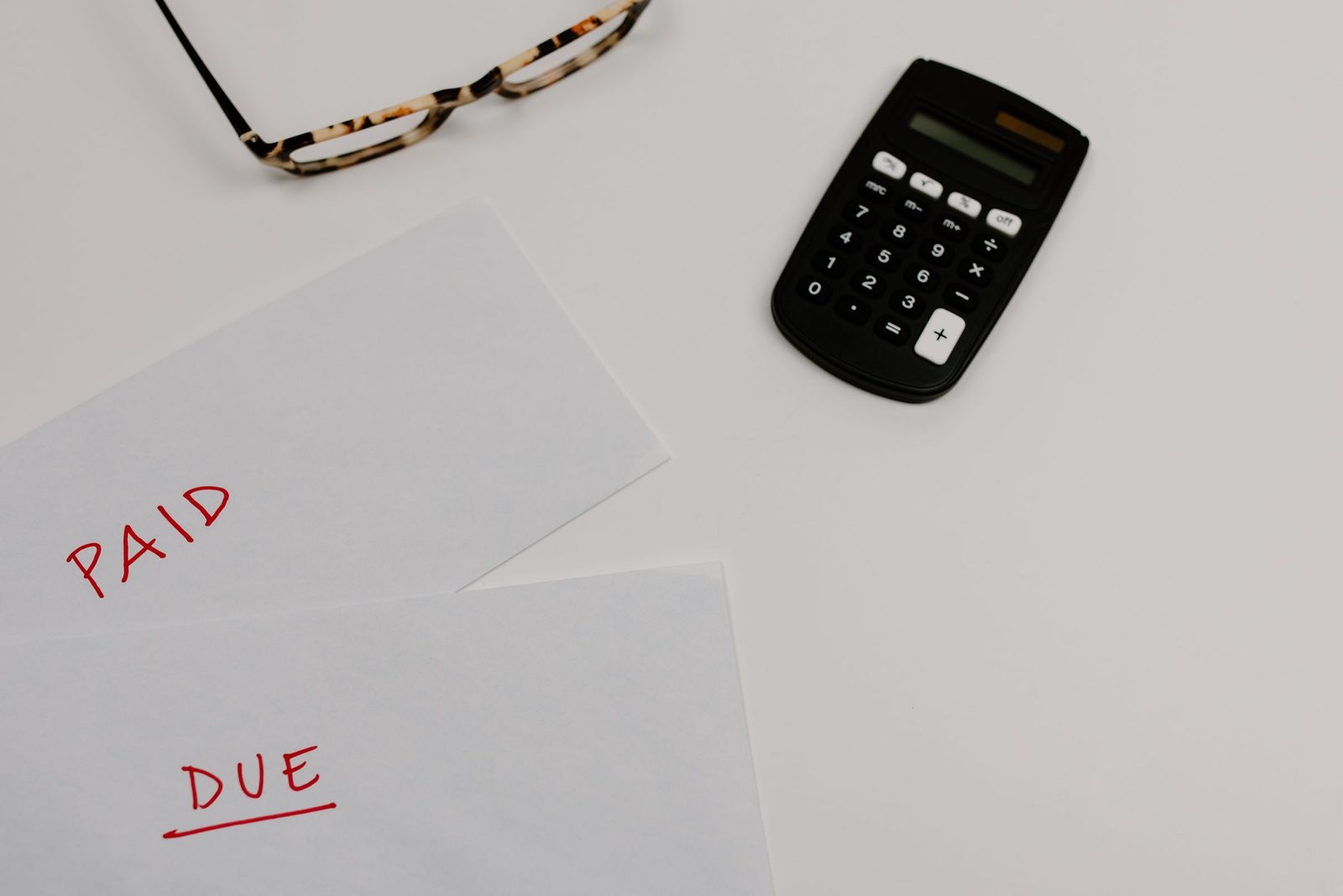 Two sheets of paper marked Paid and Due beside a calculator and glasses
