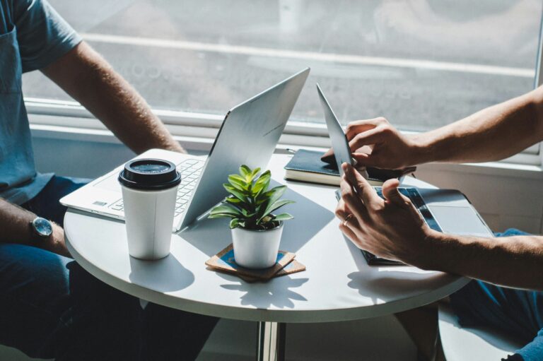 People using a laptop and a tablet at a round table with a coffee cup and a plant