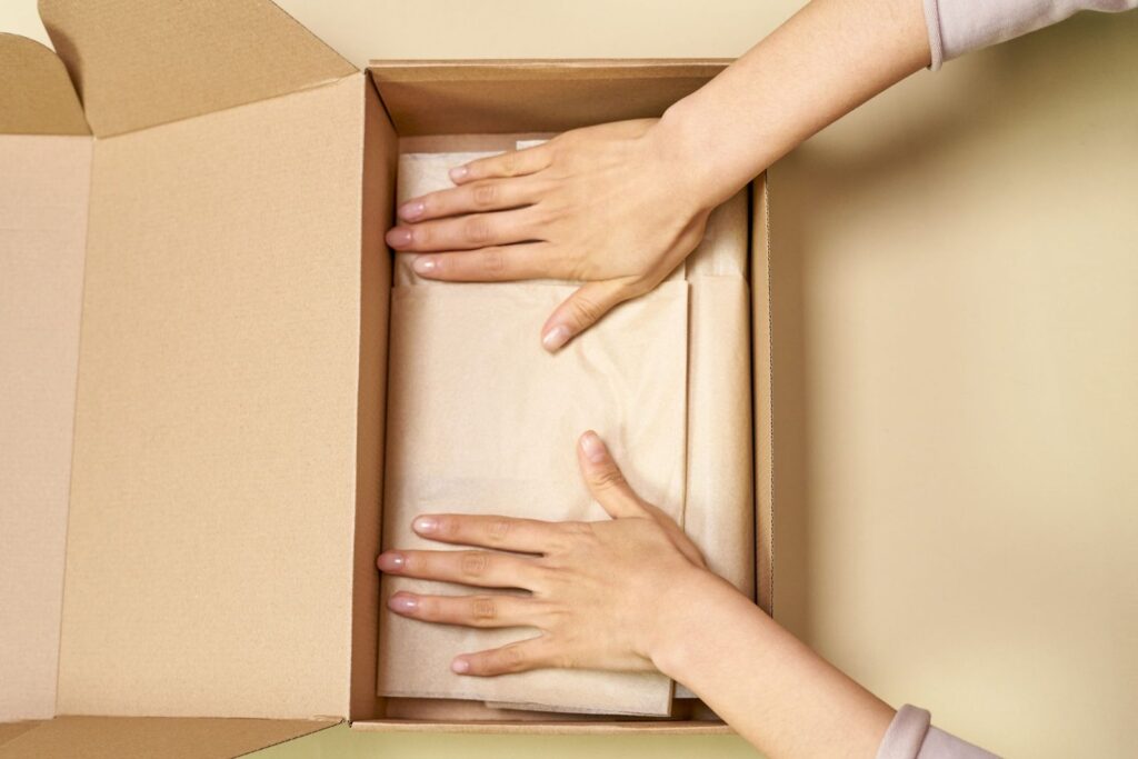 Hands packing an item wrapped in paper into a cardboard box