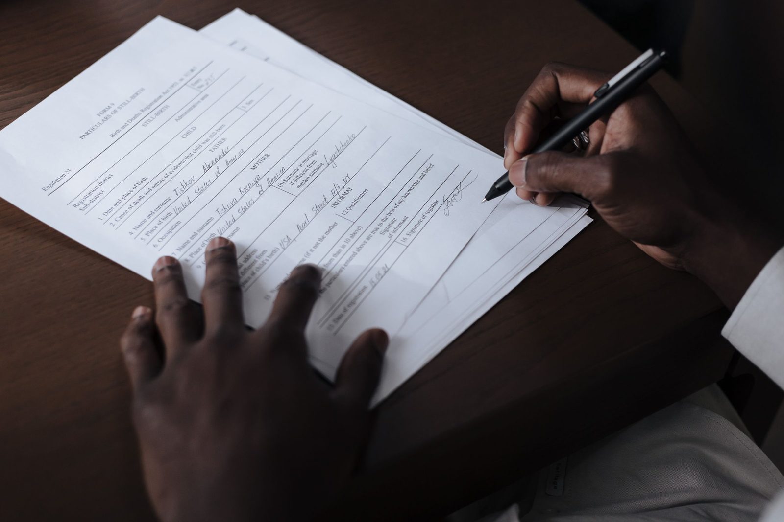 A person signing a paper form at a wooden table