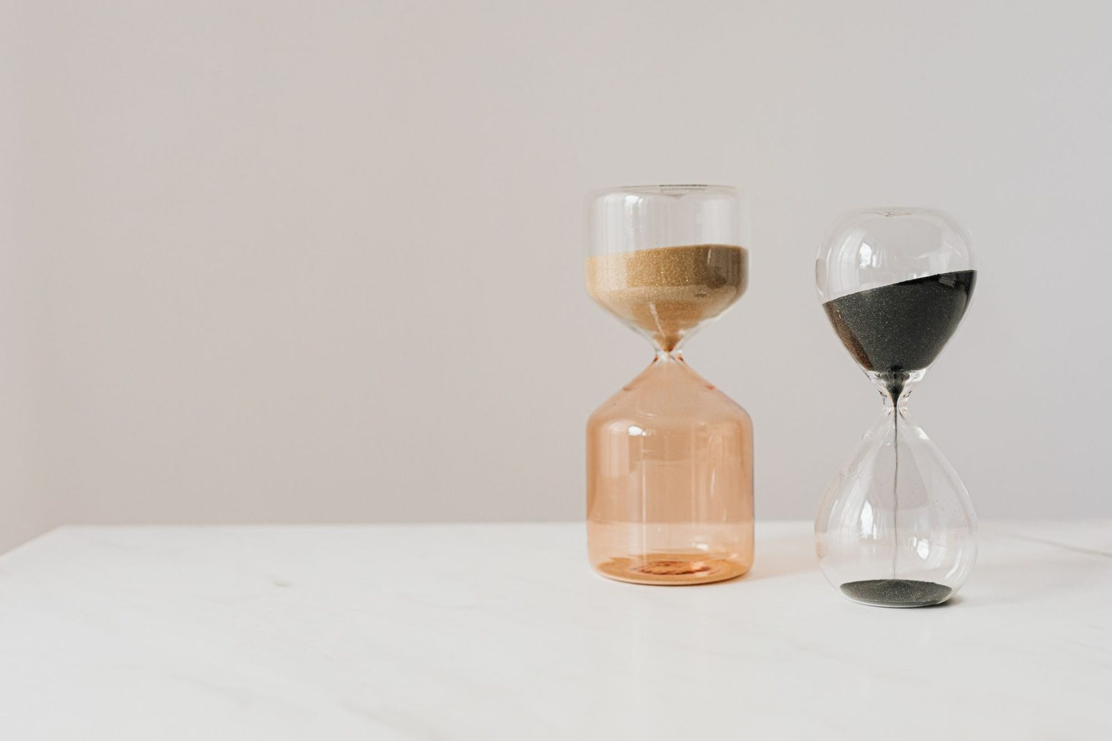 Two glass hourglasses with sand running through on a white table