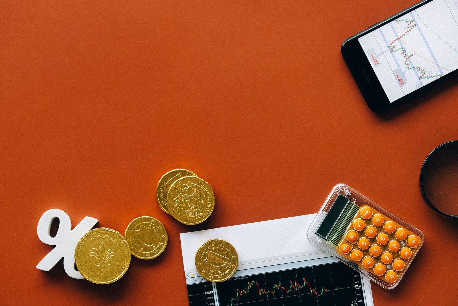 Coins, a percentage sign, a calculator and a printed chart on an orange background